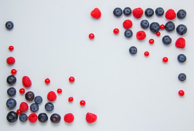 Top view raspberries in corners with blueberries, redcurrants on white background. horizontal