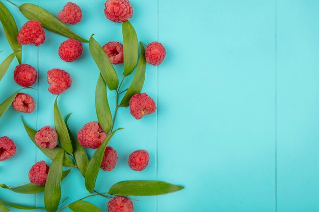 Top view of raspberries and leaves on blue surface