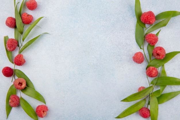 Top view of raspberries and leaves on sides on white surface