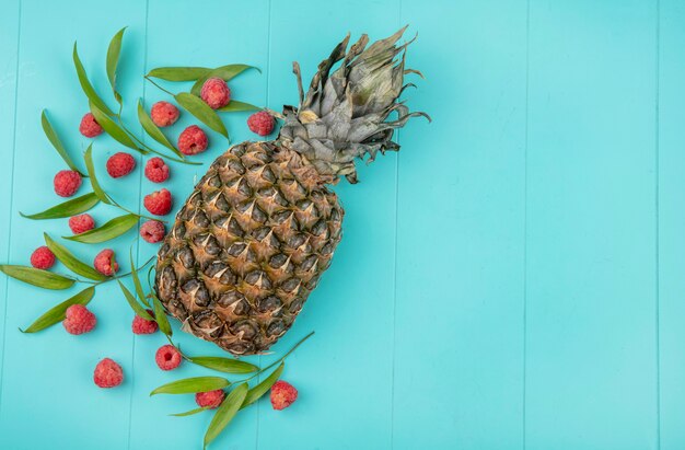 Top view of raspberries and leaves with pineapple on blue surface