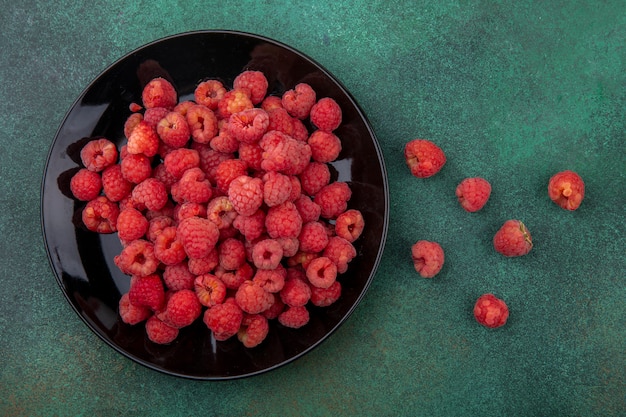 Top view of raspberries in plate and on green surface