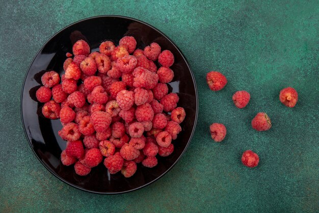 Top view of raspberries in plate and on green surface