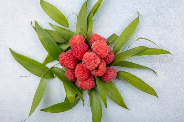 Top view of raspberries with leaves around on white surface