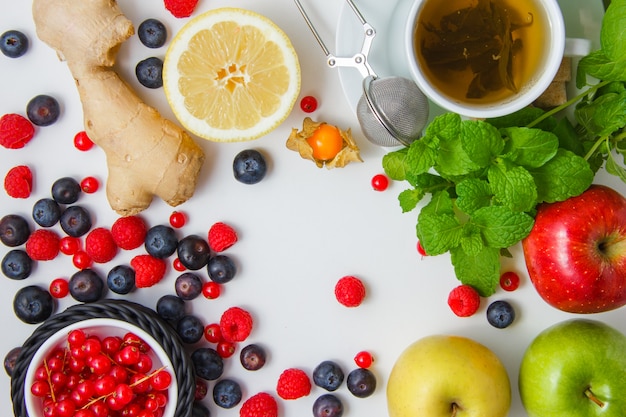 Top view raspberries with tea, apples, blueberries, redcurrants, lemon, ginger, mint leaves on white surface. horizontal