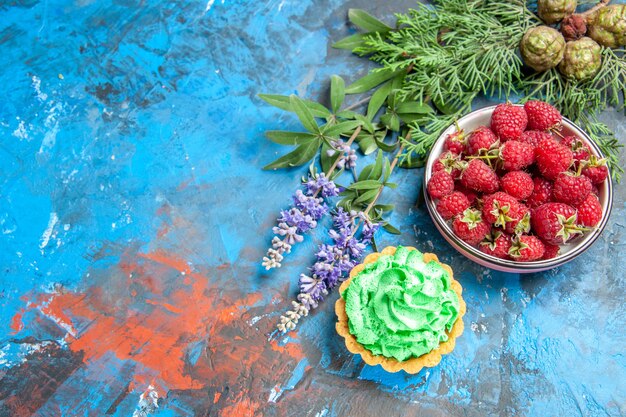 Top view of raspberry bowl and small tart on blue surface