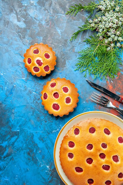 Top view of raspberry cakes on plate with fork and knife on blue surface