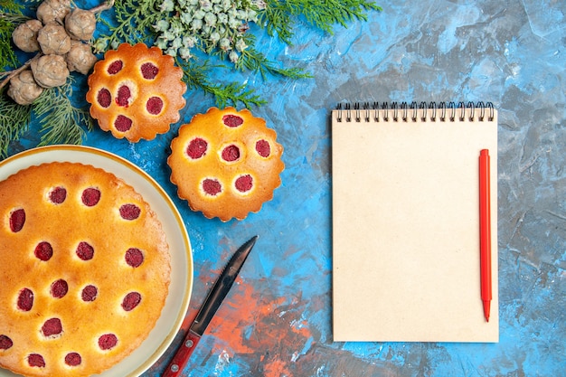 Top view of raspberry cakes with notebook on blue surface