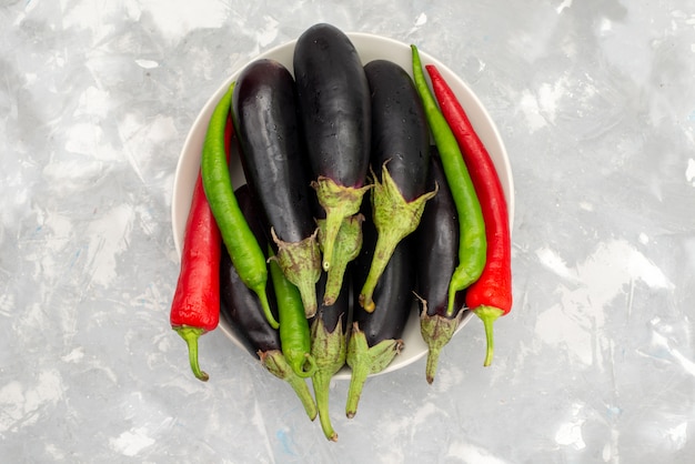 Top view raw black eggplants with peppers on the bright desk food meal vegetble spice