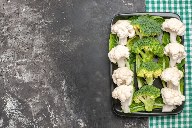 Top view raw broccoli and cauliflower on black rectangular plate on green and white checkered napkin on dark surface with copy space