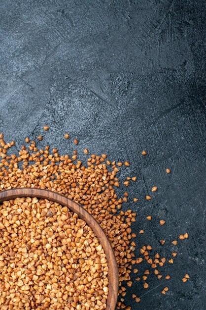 Top view raw buckwheat inside brown plate on grey space