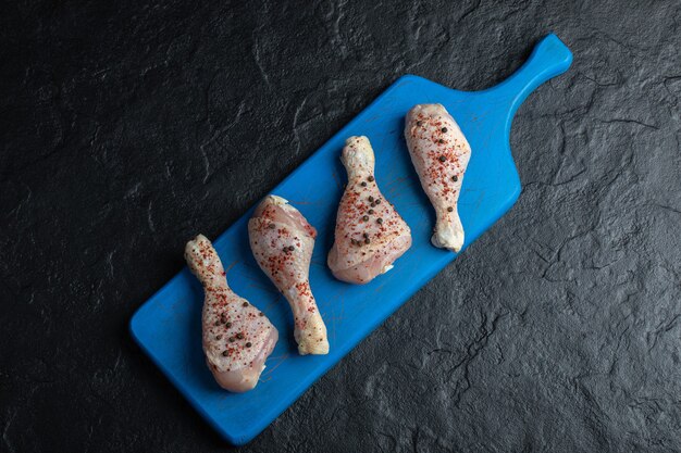 Top view raw chicken drumstick on blue wooden board.