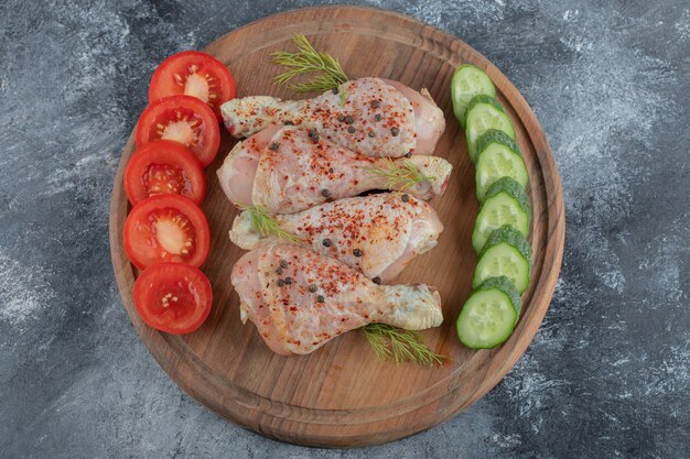 Top view raw chicken drumstick on wooden board.