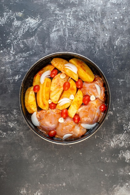 Top view of raw chicken meal with potatoes vegetables in saucepan on gray background