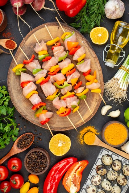 Top view raw chicken skewers on natural wood board vegetables oil bottle quail eggs on dark table