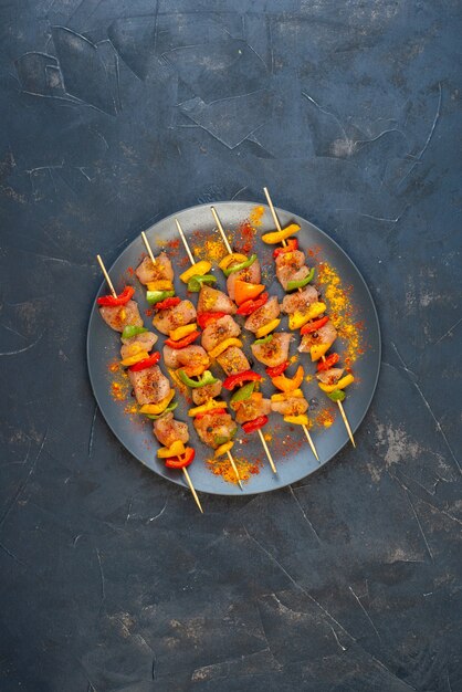 Top view raw chicken skewers with spices on wooden board on black table with copy place