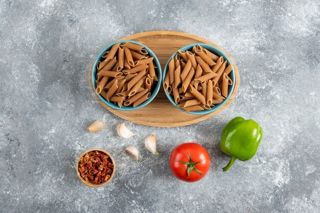 Top view of raw dietic pasta in two bowl over wooden board with vegetables.