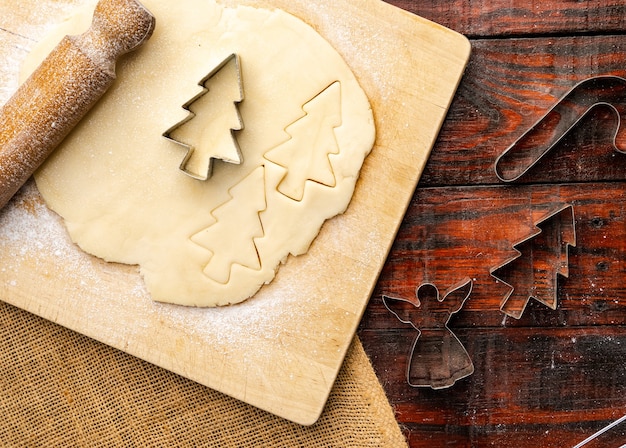 Top view of raw dough and Christmas cookie cutters on rustic kitchen table