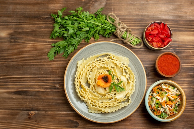 Top view raw dough designed pasta with greens and seasonings on brown background pasta dough food meal vegetable