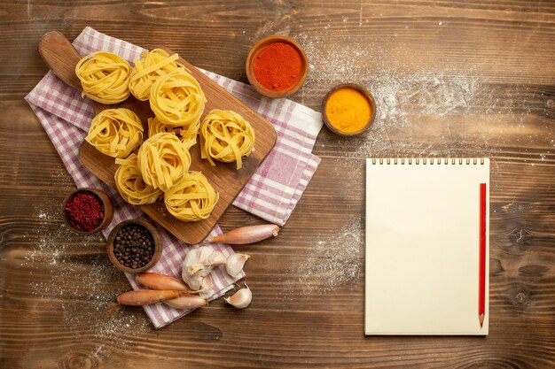 Вид сверху цветок из сырого теста в форме макарон с приправами на коричневом фоне, еда из теста, макароны