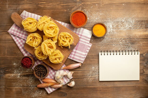 Top view raw dough flower formed pasta with seasonings on wooden background dough food pasta