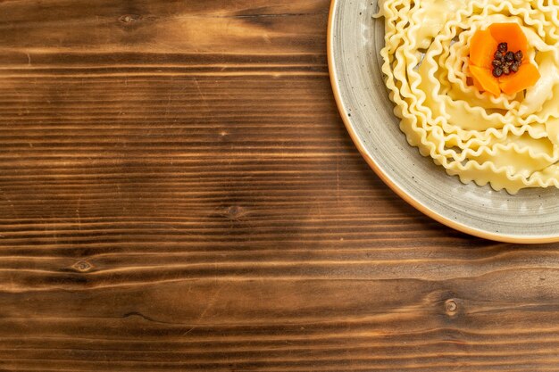 Вид сверху макароны из сырого теста, сформированные внутри тарелки на коричневом столовом тесте, пищевые макароны