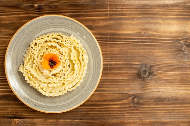 Top view raw dough pasta formed inside plate on brown table dough raw food meal pasta