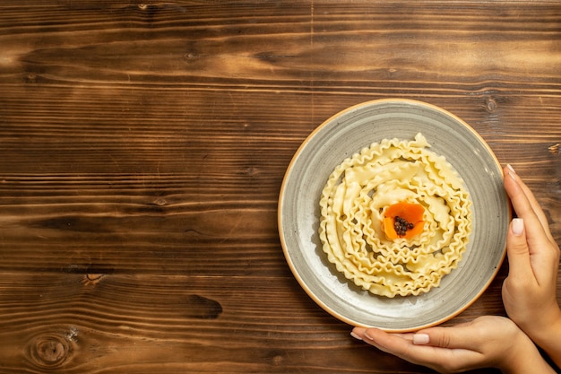 Вид сверху макароны из сырого теста, сформированные внутри тарелки на коричневом столовом тесте, сырые макароны