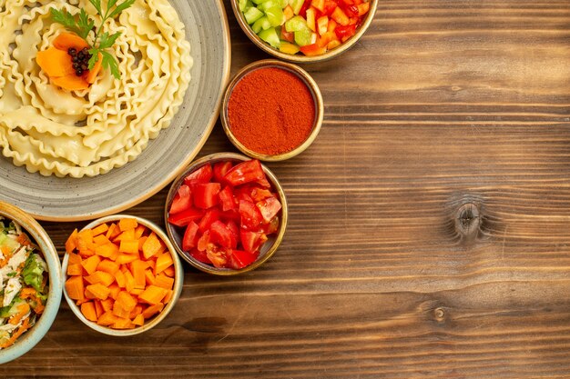 茶色のテーブル生地のローフードパスタミールに野菜と調味料で形成された上面図生生地パスタ