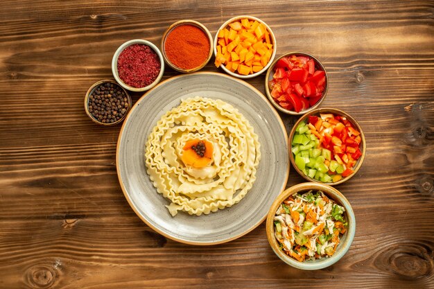 Top view raw dough pasta formed with vegetables and seasonings on brown table dough raw food pasta meal