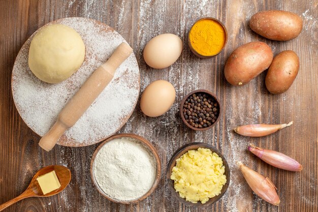 Top view raw dough piece with flour potatoes and eggs on wooden desk meal flour bake dough color