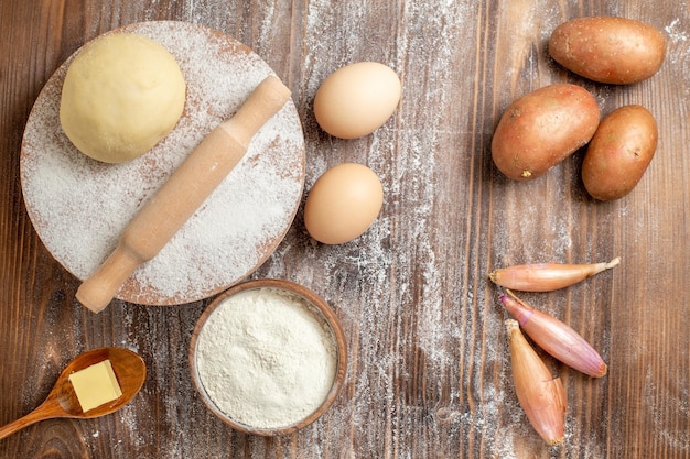 Top view raw dough piece with flour potatoes and eggs on wooden desk meal flour bake dough