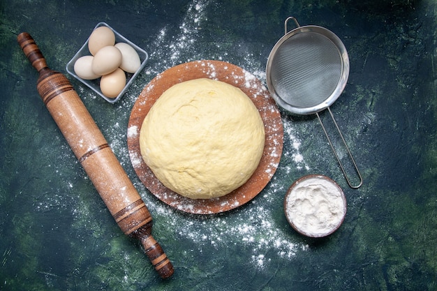 Vista dall'alto pasta cruda con farina bianca e uova su sfondo blu scuro pasticceria cuocere torta torta cruda pasta fresca al forno hotcake