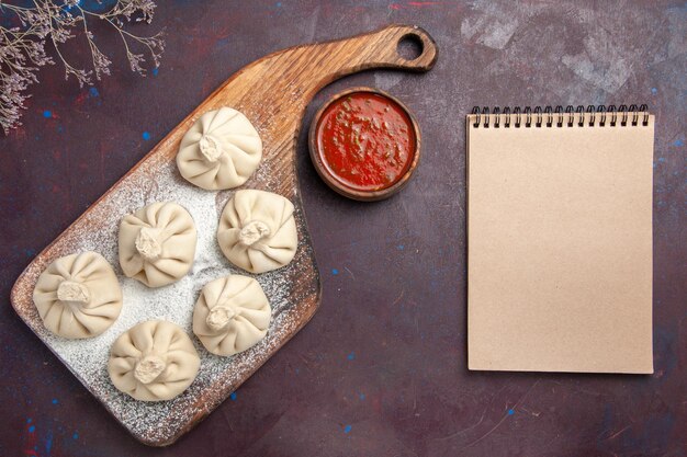 Top view of raw dumplings dough with tomato sauce on black