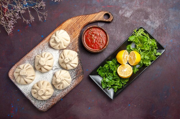 Top view of raw dumplings dough with tomato sauce and lemon on black