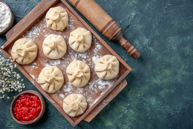 Вид сверху сырые пельмени с мясом внутри на темном фоне приготовление еды цветная мука перец блюдо тесто мясо