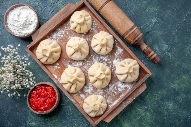 Вид сверху сырые пельмени с мясом внутри на темном столе, приготовление цветной муки, блюдо из перца, тесто, мясо