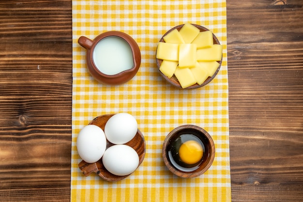 Вид сверху сырые яйца с нарезанным сыром и молоком на деревянной поверхности продукт яйца тесто еда сырая