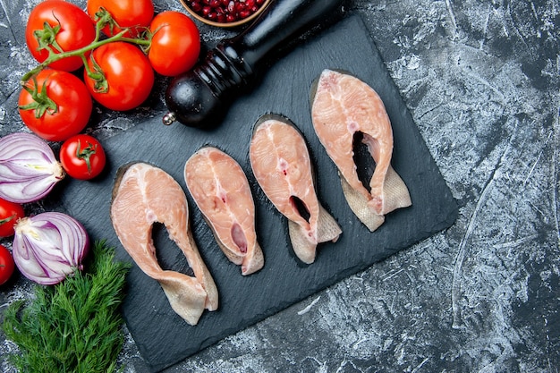 Free photo top view raw fish slices on black board dill pomegranate seeds fresh tomatoes pepper grinder on table