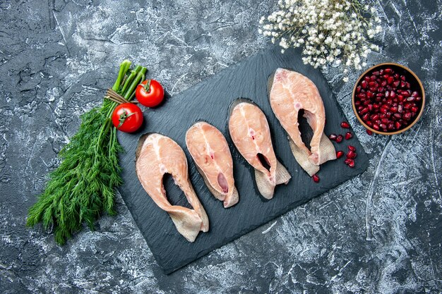 Top view raw fish slices on black board dill pomegranate seeds tomatoes on table