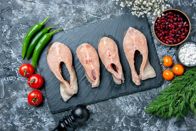 Top view raw fish slices on black board pepper grinder vegetables small white flowers on table