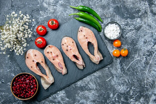 Top view raw fish slices on black board tomatoes green hot peppers on grey background