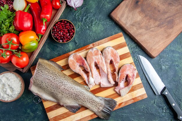 Top view raw fish slices on cutting board vegetables on wood serving board knife on kitchen table