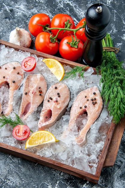 Top view raw fish slices with ice and lemon slices on wood board tomatoes garlic dill on table