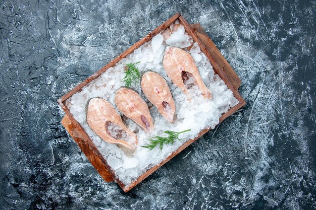 Top view raw fish slices with ice on wood board on grey background copy place