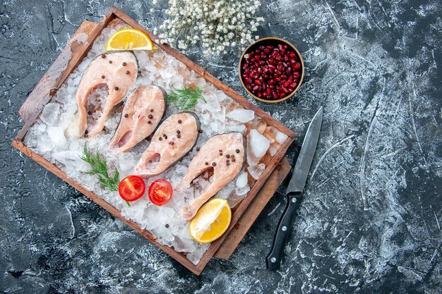 Top view raw fish slices with ice on wood board knife pomegranate seeds in small bowl on table copy place