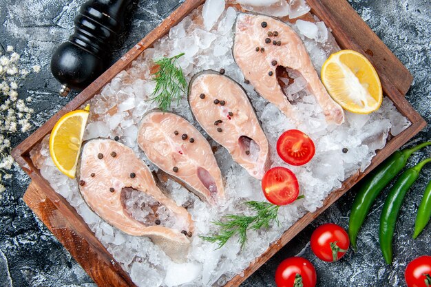 Top view raw fish slices with ice on wood board pepper grinder tomatoes on table