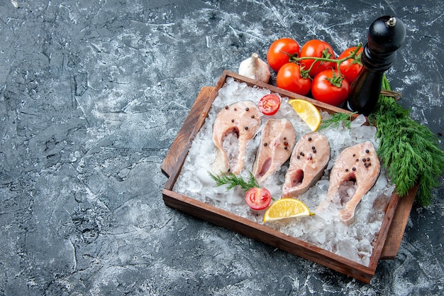 Вид сверху кусочки сырой рыбы со льдом на деревянной доске, помидоры, чеснок, укроп на столе, место для копирования