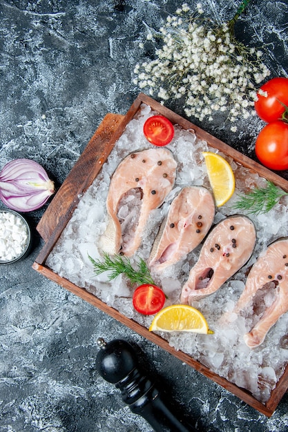 Вид сверху кусочки сырой рыбы со льдом на деревянной доске, помидоры, лук на столе