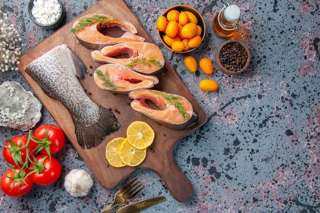 Вид сверху сырой рыбы, ломтики лимона, зелень, перец на деревянной разделочной доске и цветок продуктов на столе сине-черных цветов