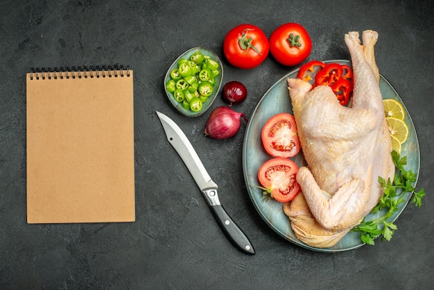 Top view raw fresh chicken inside plate with greens and vegetables on a dark background